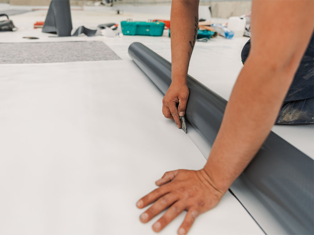 A commercial roofer cutting a TPO membrane