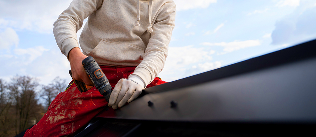 A roofer screwing in metal fastners